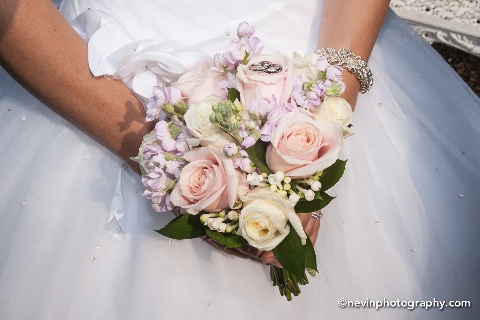 Close up of brides hands holding her flower bouquet with wedding rings on top