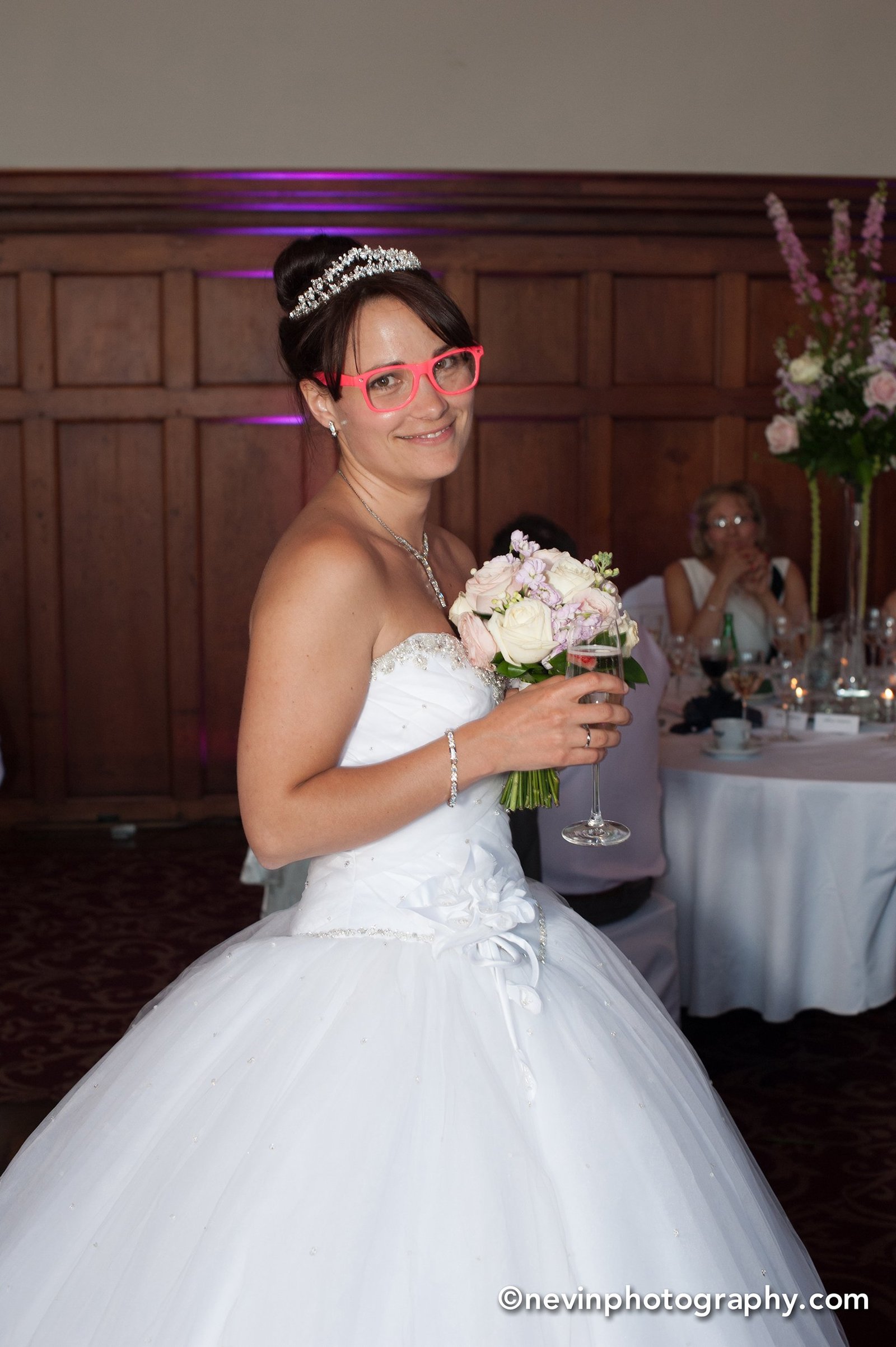 Bride smiling holding her champagne and bouquet while wearing funky glasses